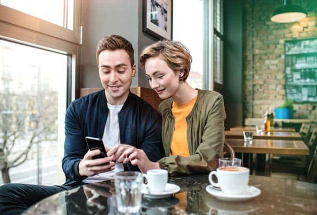 Junges Paar sitzt im Cafe innig verliebt vertraut mit Smartphone Tisch Tassen Kaffee Lifestyle Reise